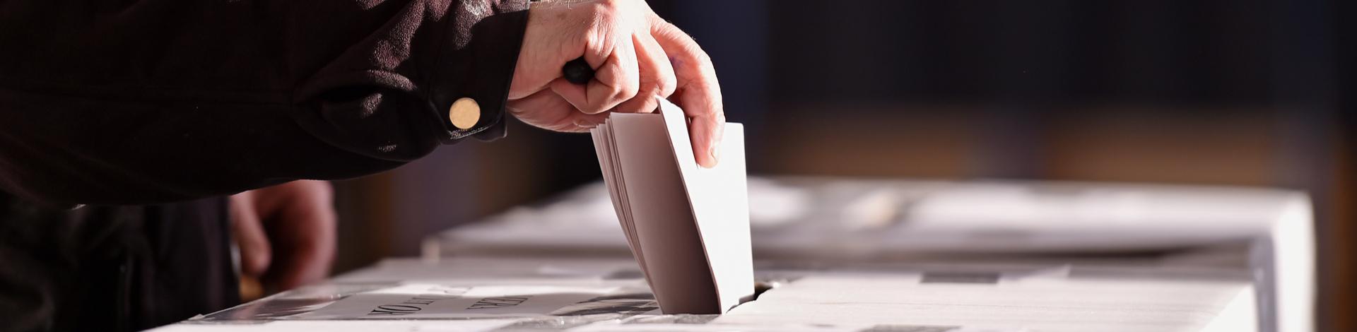 hand placing vote in ballot box at election