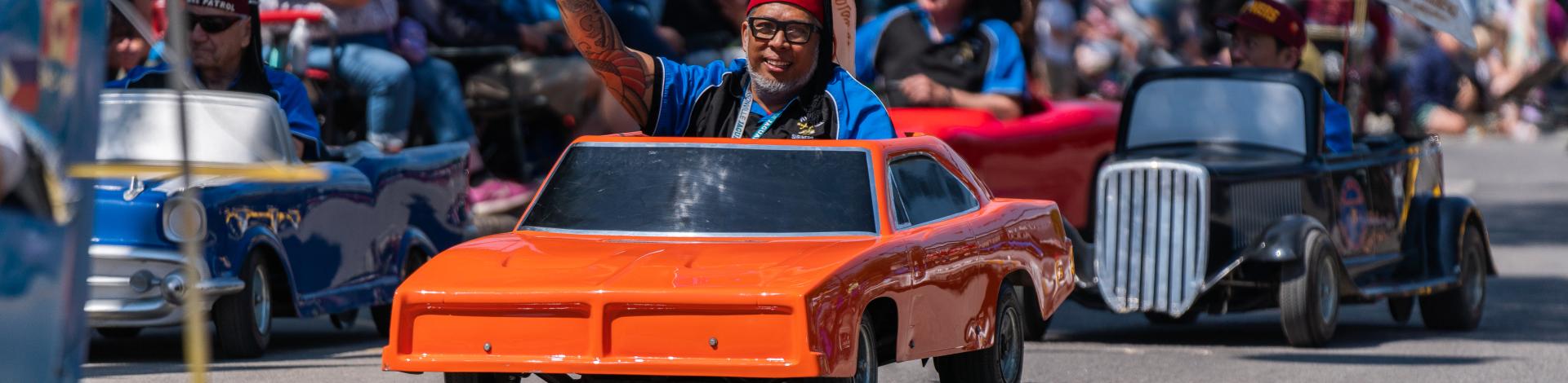 a tiny car in the okotoks parade. The man driving it is waving 