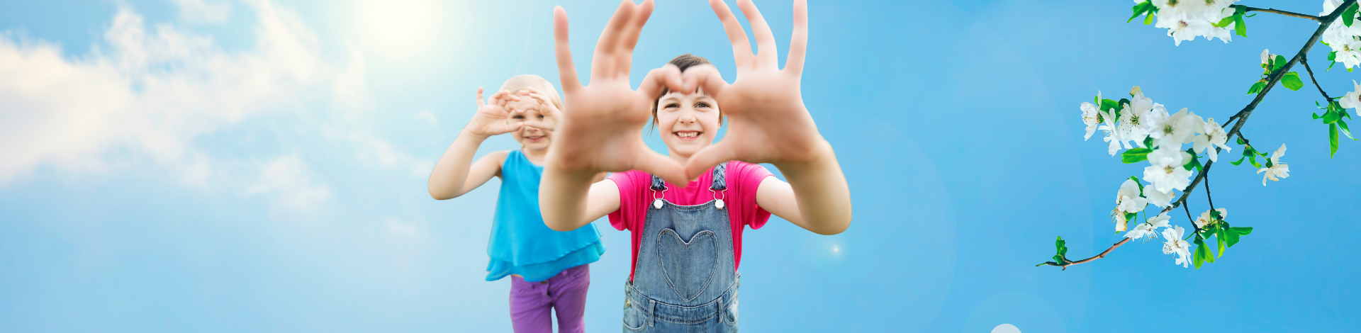 two smiling girls making a heart shape with their hands