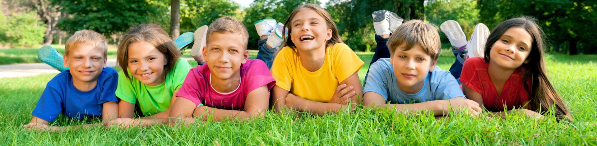 smiling children in colourful shirts lying down on stomachs in park