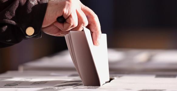 hand placing vote in ballot box at election