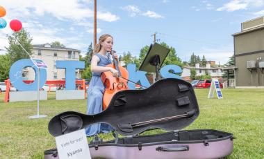 young girl plays instrument in front of Okotoks letters 