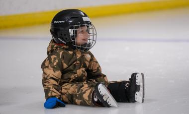 smiling child wearing helmet and skits sitting on ice