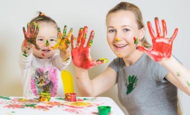 mom and daughter playing with coloured paints holding up hands