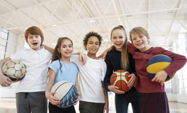 five smiling youth holding sport balls