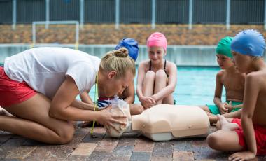 side view of female lifeguard demonstrating first aid to children