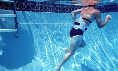 woman participating in aqua fitness attached to pool ladder using tether