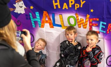 three young boys stand in front of a happy halloween sign 