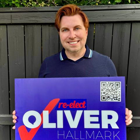 Man smiling in front of fence holding an election sign