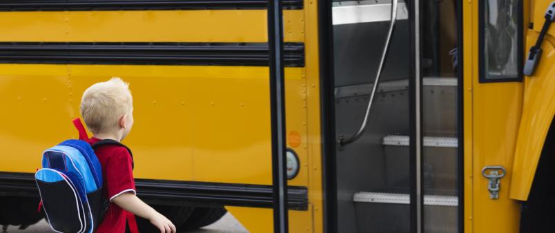 young boy stands in front of a yellow school bus with a blue backpack on 