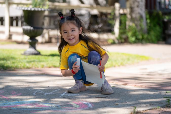 smiling little girl drawing with chalk on the sidewalk