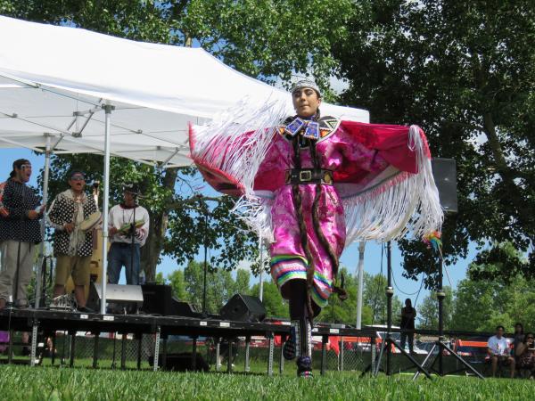 Canada Day celebrations with an Indigenous dancer in brigh pink regalia and drummers in the background