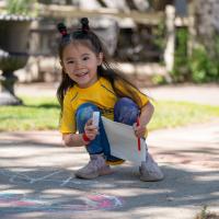 smiling little girl drawing with chalk on the sidewalk