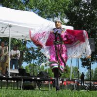 Canada Day celebrations with an Indigenous dancer in brigh pink regalia and drummers in the background