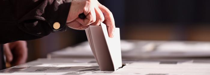 hand placing vote in ballot box at election