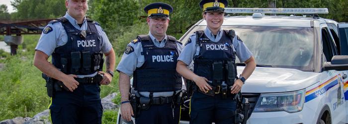 Three RCMP officers standing in front of an RCMP cruiser
