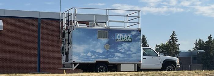 a monitoring truck is parked outside of a building with a long antenna out the top